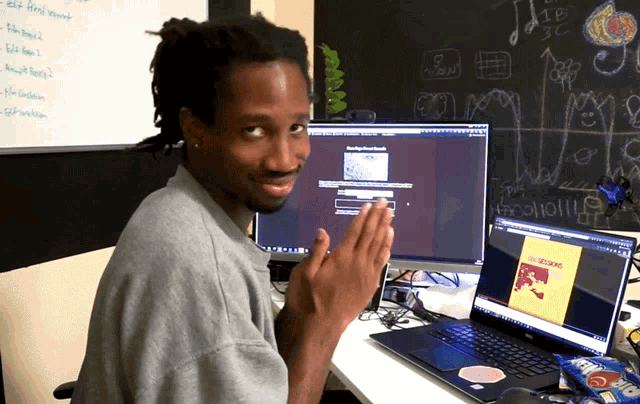a man sitting at a desk with a computer and a laptop with the word scream on it