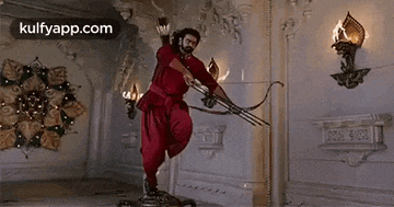 a man in a red dress is holding a bow and arrow in a room .