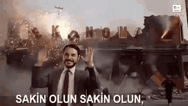 a man in a suit and tie is waving in front of a burning building with the words sakin olsun written below him