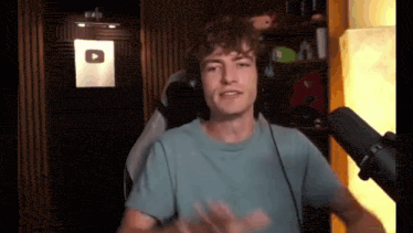 a young man wearing headphones and a blue shirt is standing in front of a microphone .