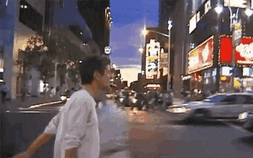 a man is walking down a city street at night with a car driving by .