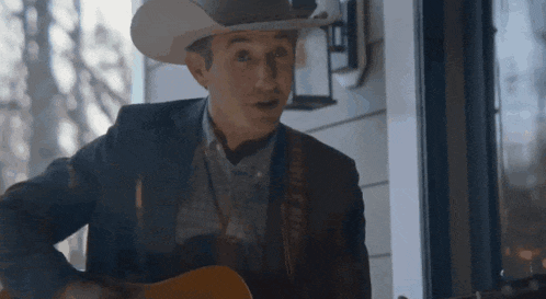 a man in a cowboy hat is playing a guitar on a porch