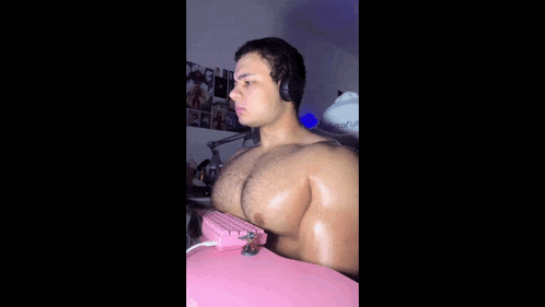 a shirtless man wearing headphones is sitting at a pink desk with a keyboard .