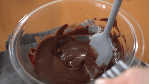 a person is mixing chocolate in a glass bowl