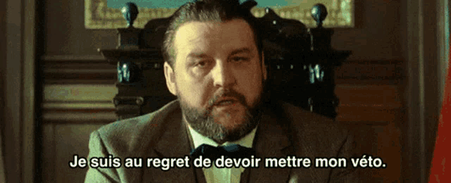 a man with a beard is sitting in a chair with the words je suis au regret de devoir mettre mon veto below him
