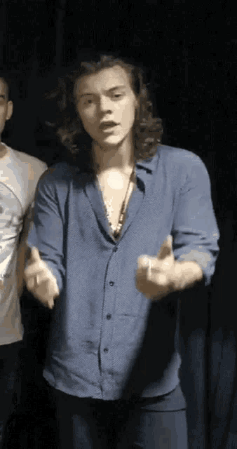 a man with long hair is wearing a blue shirt and giving a middle finger