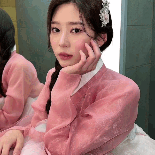 a woman in a pink dress with a flower in her hair looks at the camera