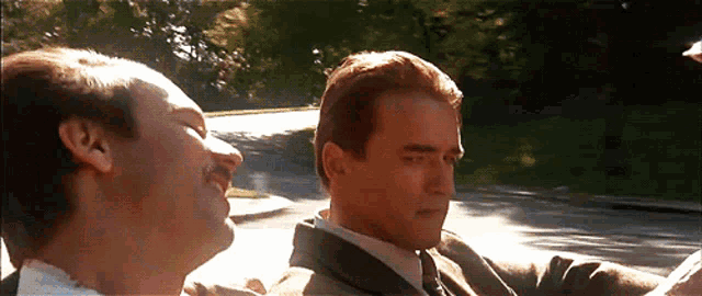 two men in suits and ties are driving down a street