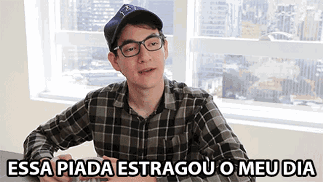 a man wearing glasses and a baseball cap is sitting at a table with the words essa piada estragou o meu dia below him