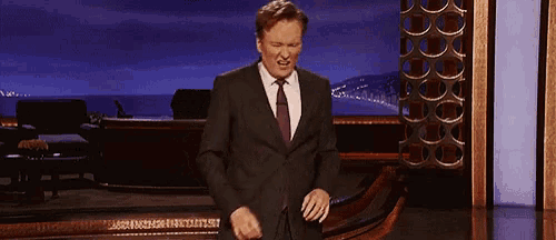 a man in a suit and tie stands on a stage with his hands folded