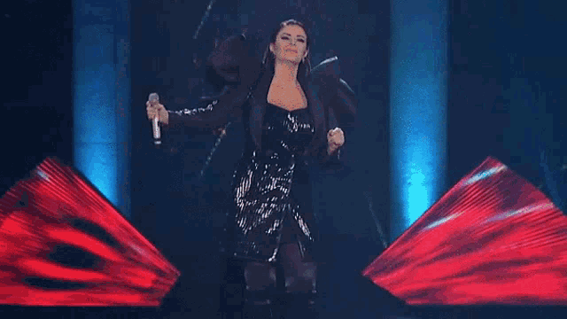 a woman in a sequined dress is singing into a microphone on a stage .