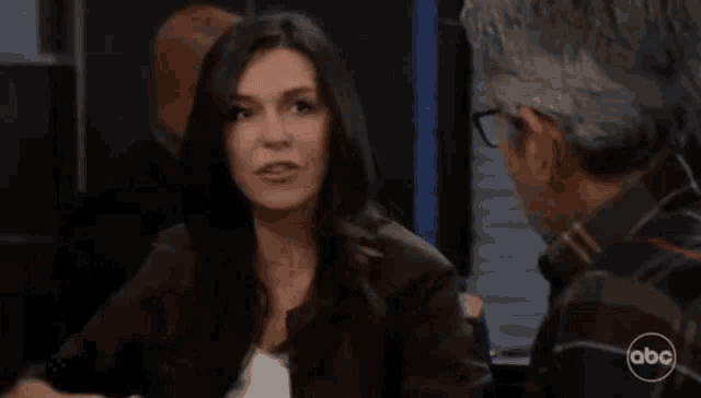 a woman in a brown jacket is talking to a man in a plaid shirt with abc written on it