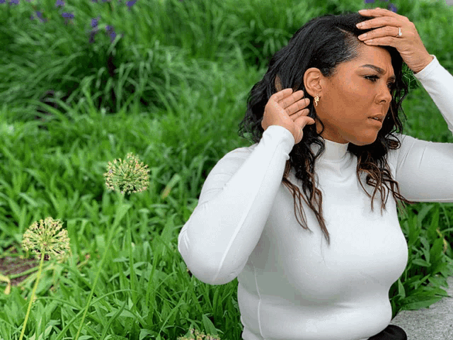 a woman wearing a white turtleneck is standing in the grass