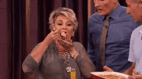 a woman is eating a piece of food while a man holds a plate of food .