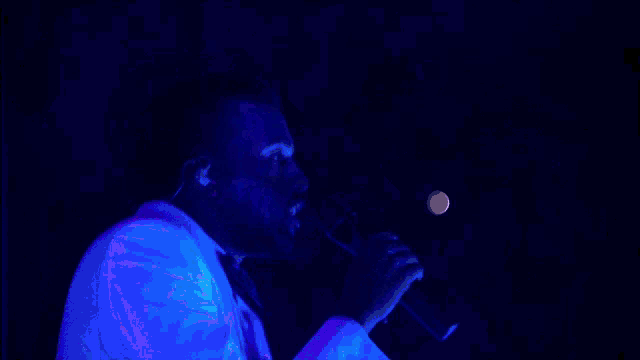 a man singing into a microphone in a purple light