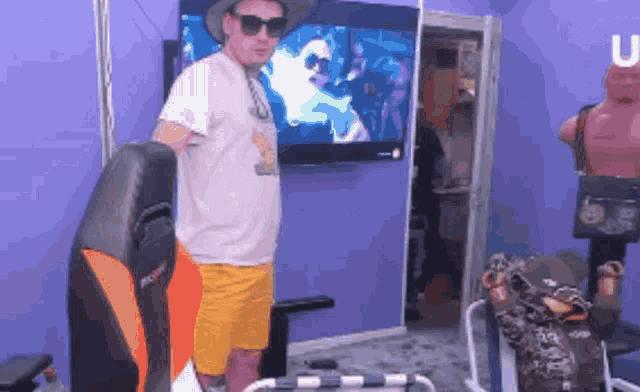 a man in a hat and sunglasses stands in front of a tv