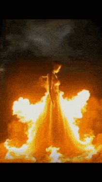a woman in a long dress is surrounded by flames .