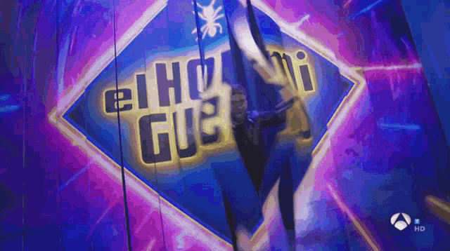 a person is hanging from a rope in front of a sign that says " el hot gue "