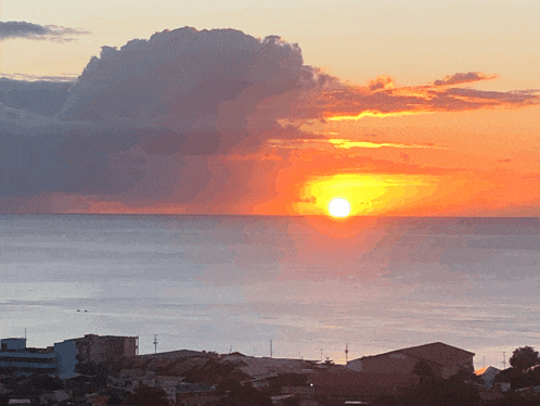 a sunset over the ocean with a cloud in the sky