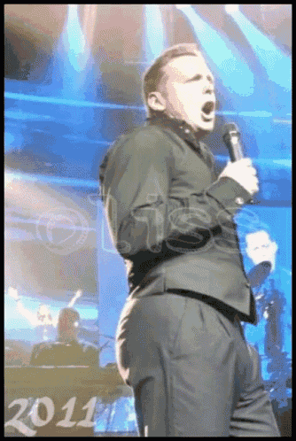 a man in a suit singing into a microphone with the year 2011 in the background