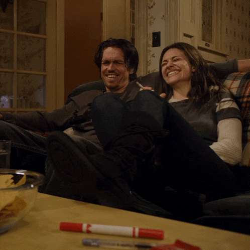 a man and woman sit on a couch laughing
