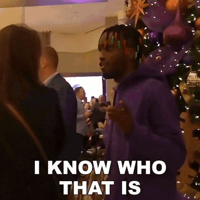 a man in a purple hoodie says " i know who that is " in front of a crowd