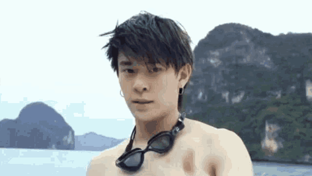 a young man without a shirt is wearing goggles and standing on a beach .