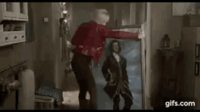 a man in a red shirt is standing next to a painting of a man .