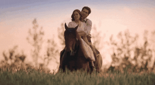 a man and a woman are riding a horse through a field .