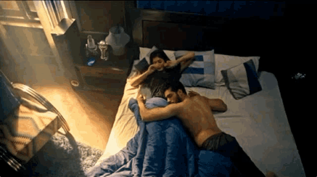 a man and woman laying on a bed with a blue blanket