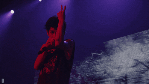 a person giving a peace sign in front of a purple background with the letter d on it