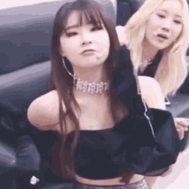 two women are sitting next to each other on a couch . one of the women is wearing a choker necklace .