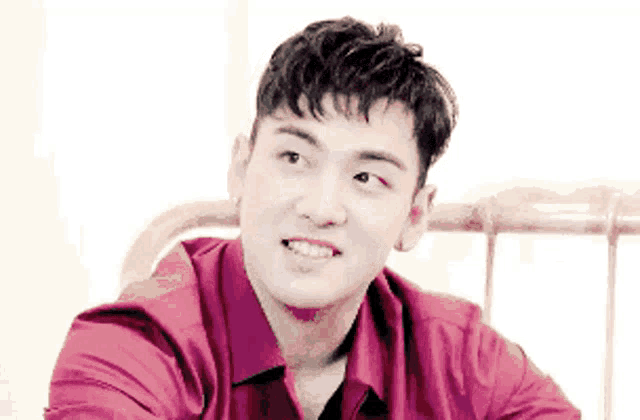 a young man in a red shirt is sitting on a bed .