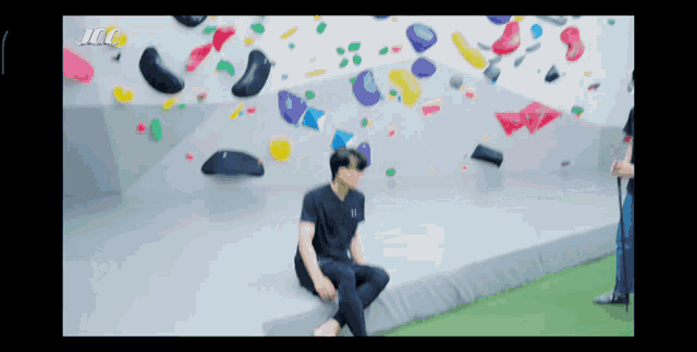 a man sits on a ledge in front of a climbing wall that says icc on the bottom