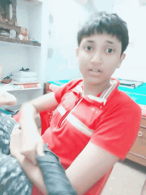 a young boy wearing a red shirt with a white stripe on the collar