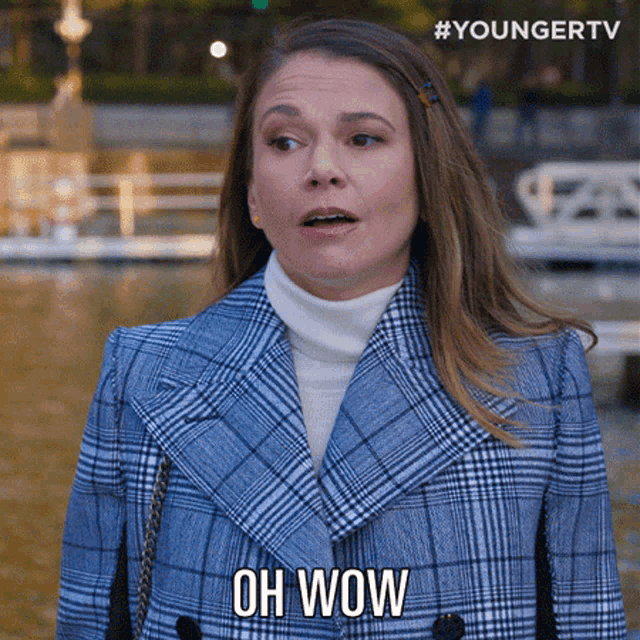 a woman wearing a plaid coat and a white turtleneck says oh wow