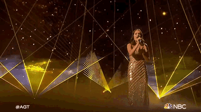 a woman is singing on a stage with a nbc logo in the background