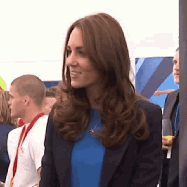 a woman wearing a blue shirt and a black jacket is standing in a crowd