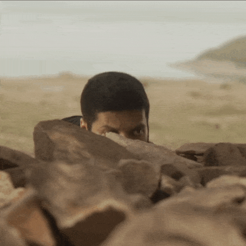 a man hiding behind a pile of rocks with his eyes closed