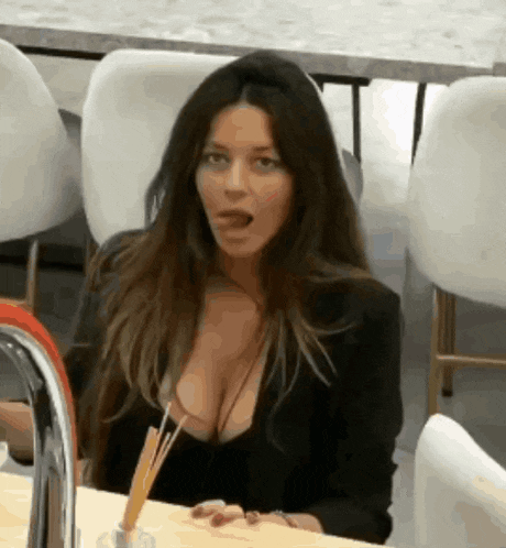 a woman with a very large breast is sitting at a table with her tongue out
