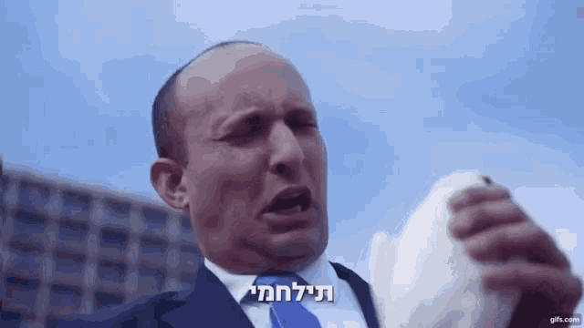 a man in a suit and tie holds a piece of paper in front of his face with a blue sky in the background
