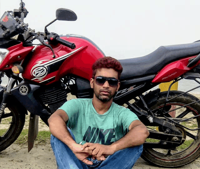 a man wearing a nike shirt sits in front of a yamaha motorcycle