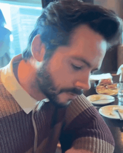a man with a beard is sitting at a table with plates of food on it