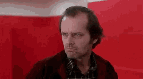 a man in a plaid shirt and a red jacket is standing in front of a red wall .