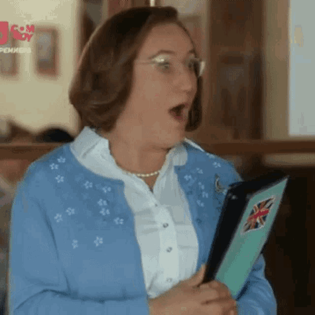 a woman in a blue sweater is holding a folder with a british flag on it