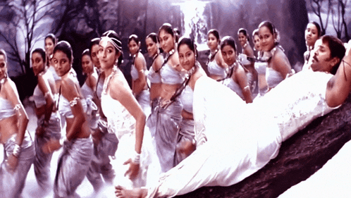 a man is laying on a tree branch with a group of women dancing around him