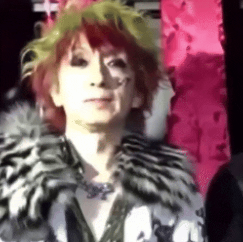 a woman with red hair and green hair is wearing a fur coat .