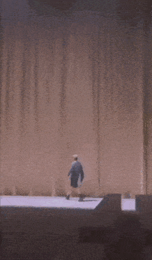 a man in a blue shirt and shorts is standing behind a brown curtain