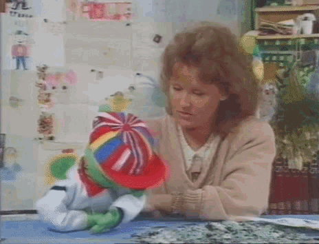 a woman is sitting at a table with a colorful hat on a puppet