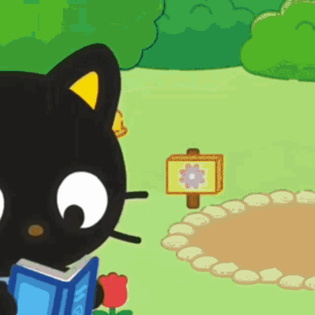 a black cat is reading a book in a garden next to a sign with a flower on it .